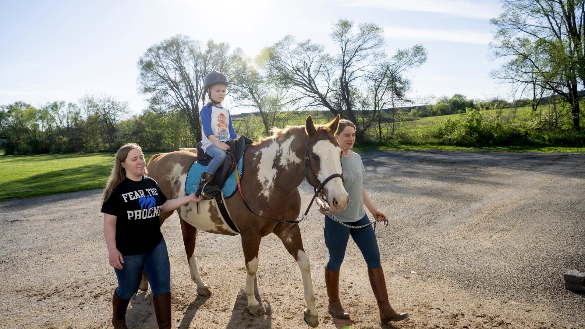 Two equestrian students walking a horse with a child riding