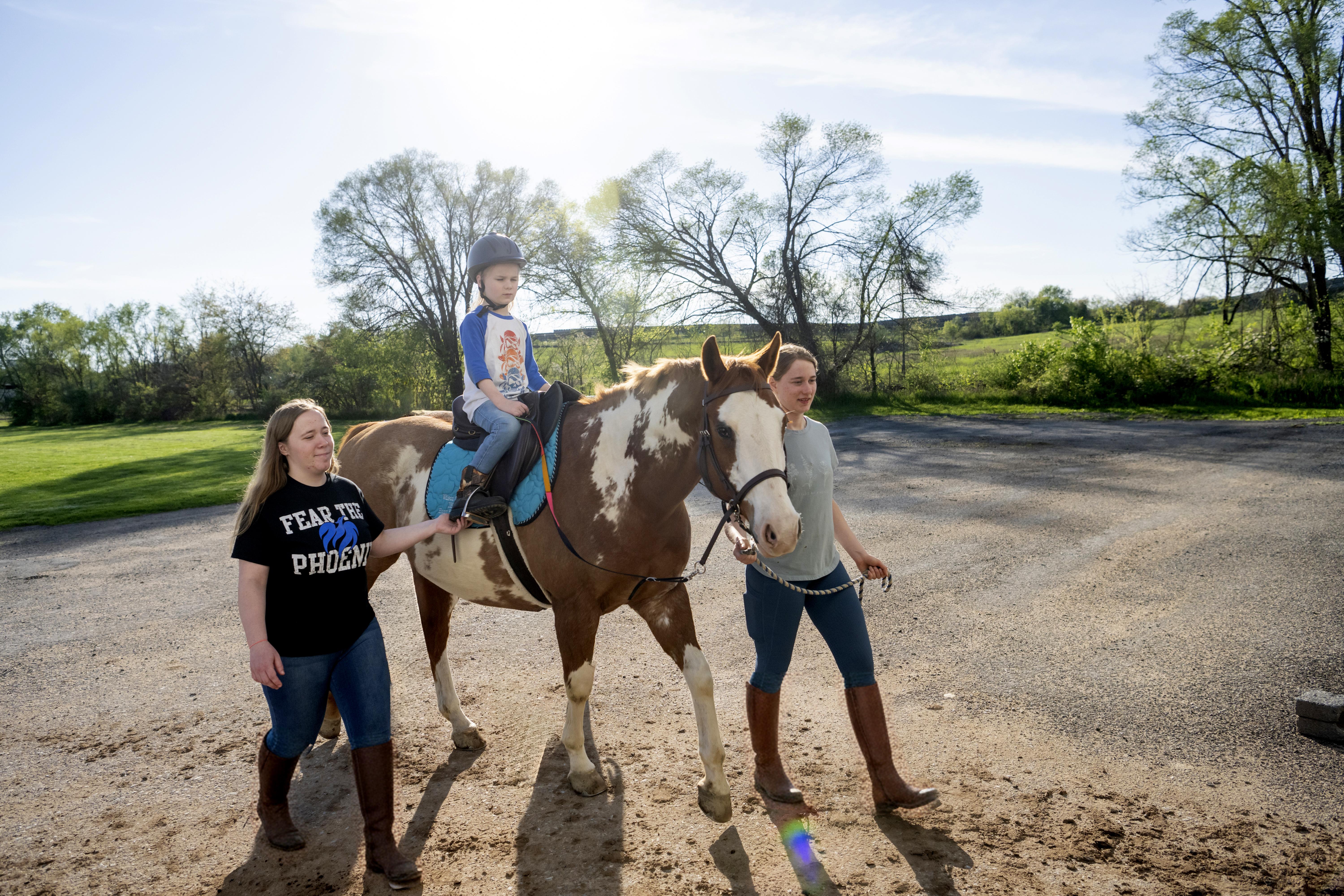 Two equestrian students walking a horse with a child riding